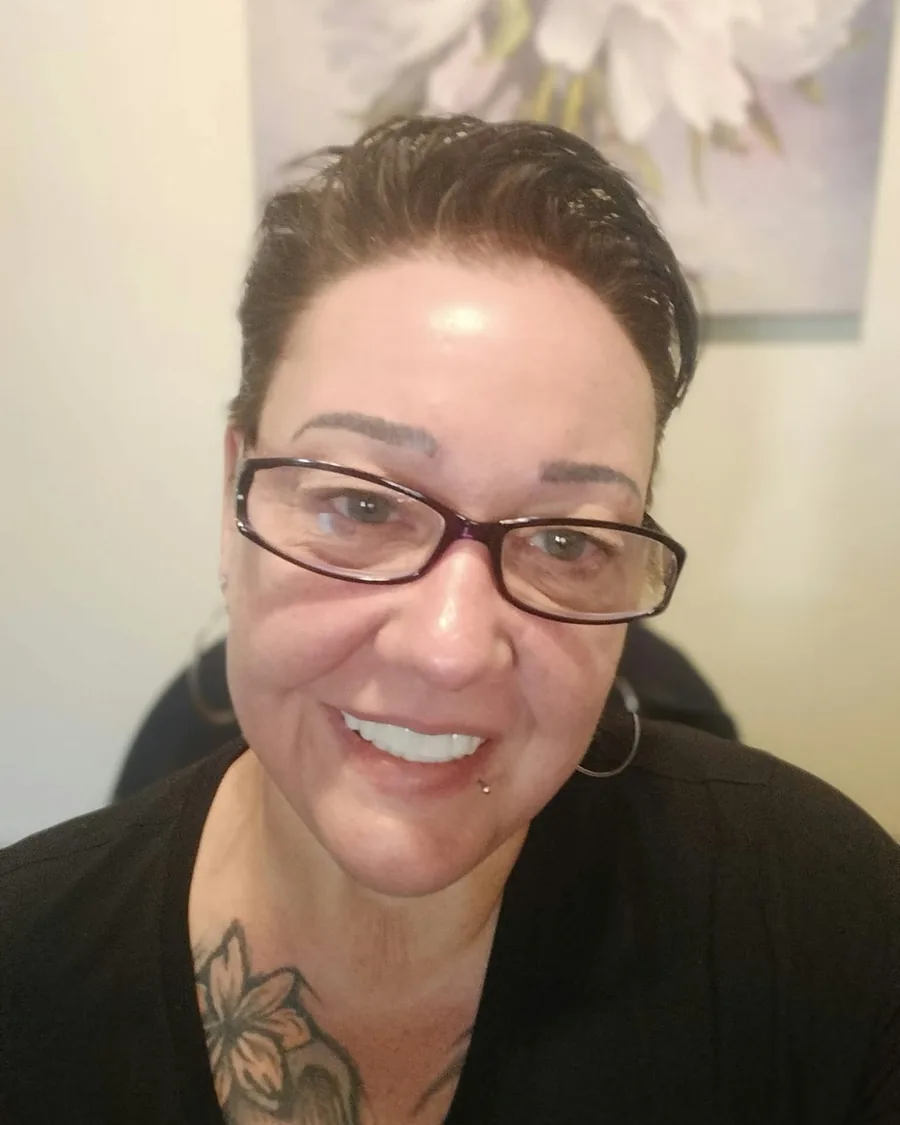 Stacy Tennent smiling, in glasses, with a flower tattoo on her chest