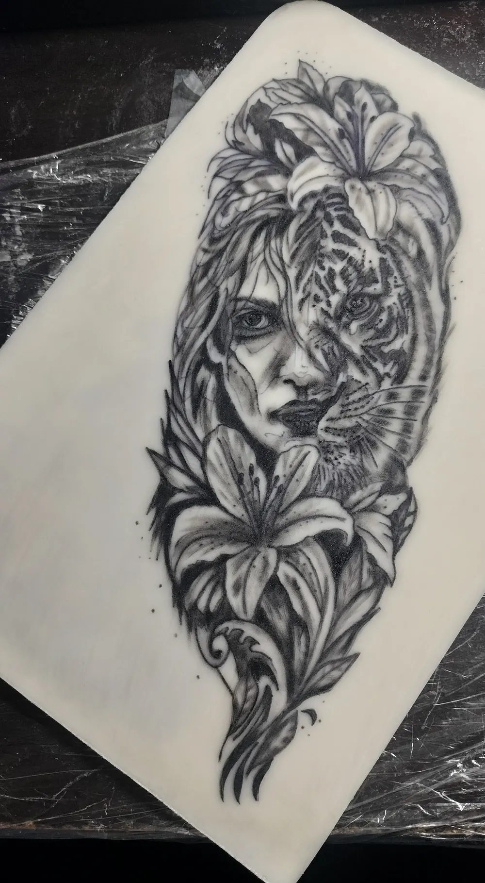 A woman whose face turns into a tiger, framed by lilies, black and grey on practice skin